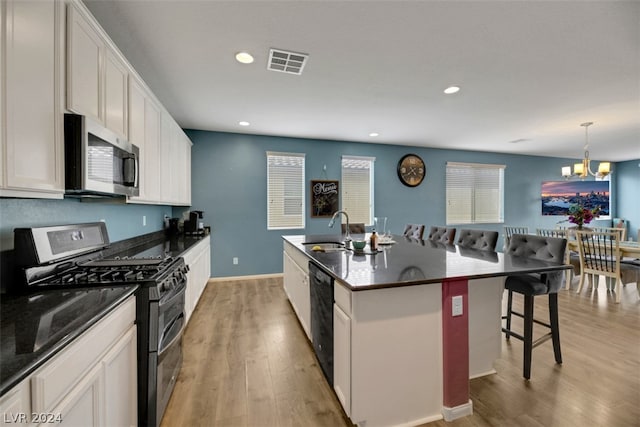 kitchen with a notable chandelier, white cabinets, a kitchen island with sink, light hardwood / wood-style floors, and appliances with stainless steel finishes