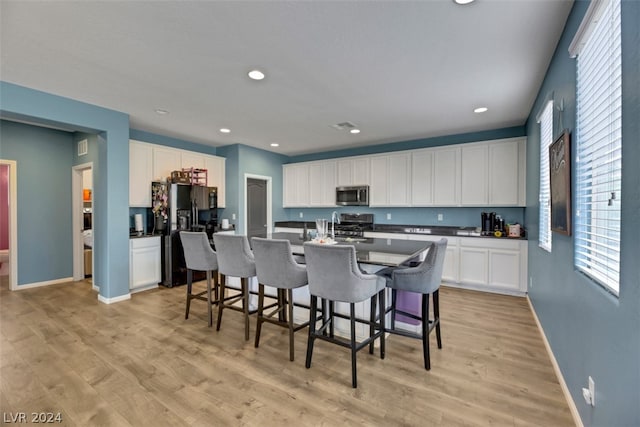 kitchen featuring white cabinetry, stainless steel appliances, light hardwood / wood-style floors, and a center island with sink