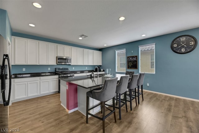 kitchen with white cabinetry, light wood-type flooring, stainless steel appliances, and a kitchen island with sink