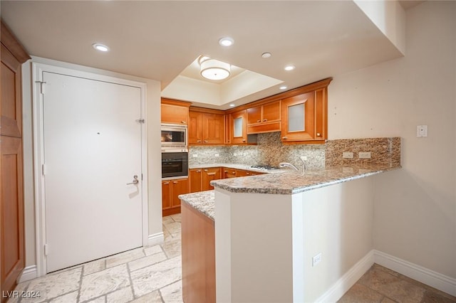 kitchen featuring stainless steel microwave, decorative backsplash, light stone countertops, black oven, and kitchen peninsula