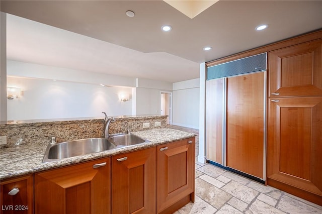 kitchen featuring light stone countertops, sink, and paneled refrigerator