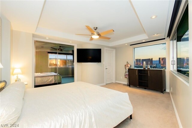 bedroom with ceiling fan, light carpet, and a tray ceiling