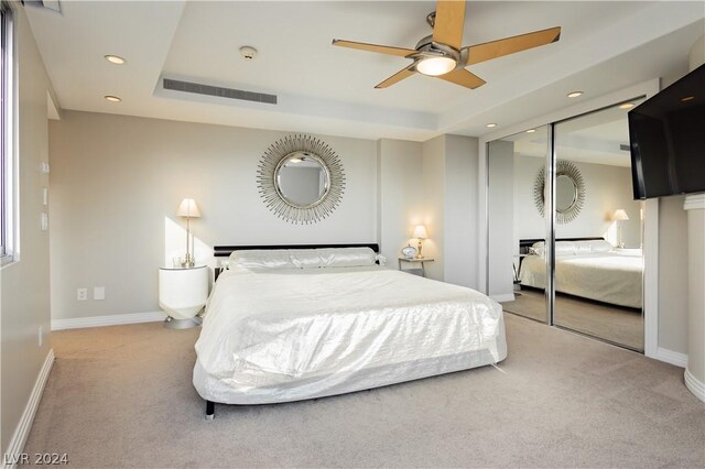 carpeted bedroom featuring a tray ceiling, ceiling fan, and a closet