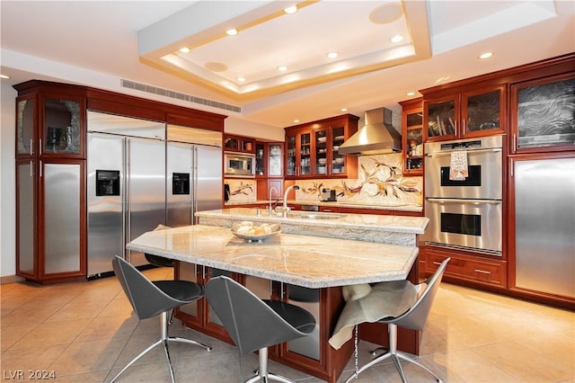 kitchen with light tile patterned floors, wall chimney exhaust hood, a tray ceiling, and built in appliances