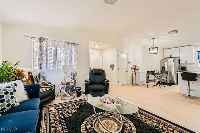 living room with an inviting chandelier, vaulted ceiling, and light wood-type flooring