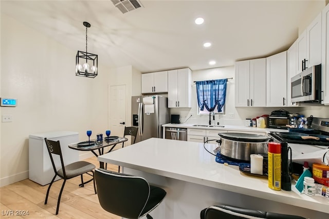 kitchen with appliances with stainless steel finishes, decorative light fixtures, light hardwood / wood-style floors, white cabinetry, and sink