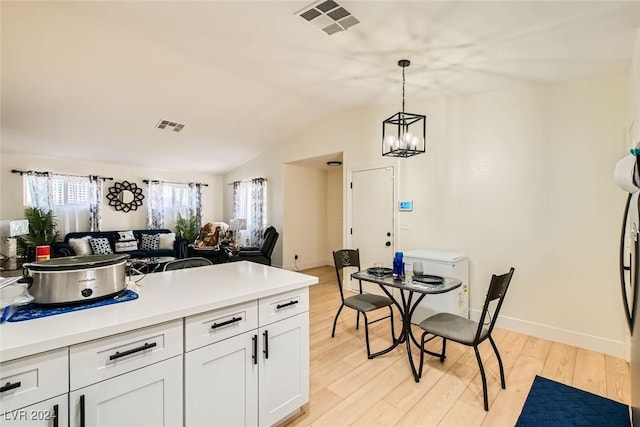 kitchen with hanging light fixtures, vaulted ceiling, white cabinets, and light wood-type flooring