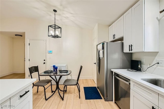 kitchen with hanging light fixtures, stainless steel appliances, white cabinets, a chandelier, and light wood-type flooring