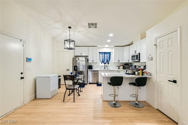 kitchen featuring appliances with stainless steel finishes, pendant lighting, white cabinets, and light hardwood / wood-style flooring