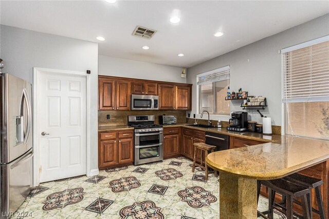 kitchen with appliances with stainless steel finishes, a breakfast bar area, sink, kitchen peninsula, and decorative backsplash