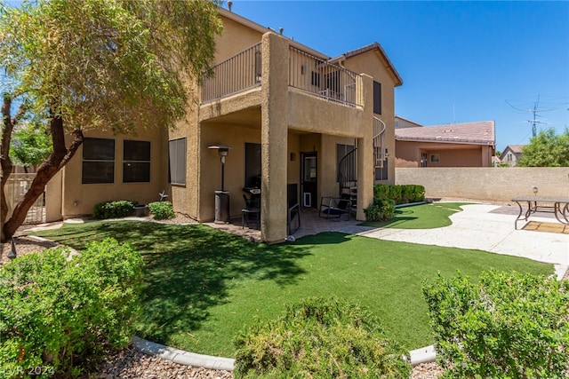 back of property featuring a balcony, a patio area, and a yard