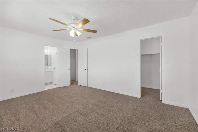 unfurnished bedroom featuring carpet flooring, a walk in closet, ceiling fan, ensuite bath, and a closet