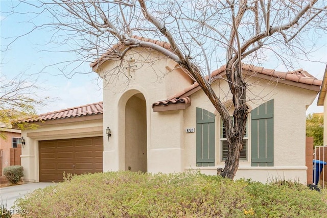 mediterranean / spanish-style house with a garage, a tiled roof, concrete driveway, and stucco siding