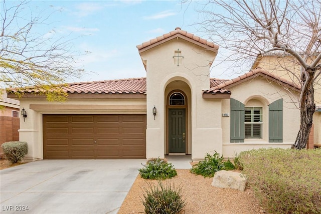 mediterranean / spanish-style home with a garage, concrete driveway, a tiled roof, and stucco siding