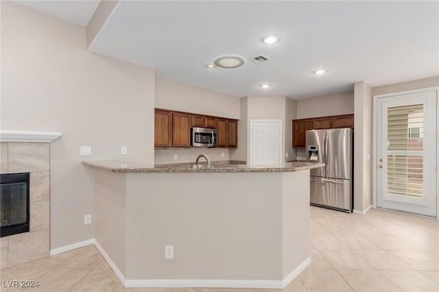 kitchen featuring light stone counters, a tile fireplace, a peninsula, visible vents, and appliances with stainless steel finishes