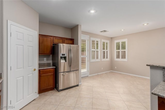 kitchen with plenty of natural light, light stone counters, brown cabinets, and stainless steel fridge with ice dispenser