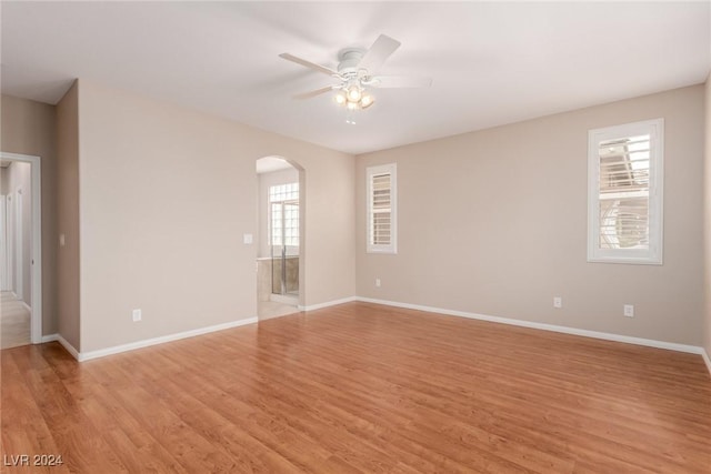 empty room with light wood-style floors, arched walkways, baseboards, and a ceiling fan