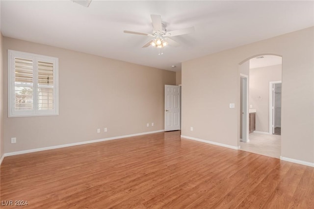 unfurnished room featuring arched walkways, light wood-type flooring, a ceiling fan, and baseboards