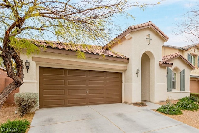 mediterranean / spanish-style home featuring a garage, a tile roof, concrete driveway, and stucco siding