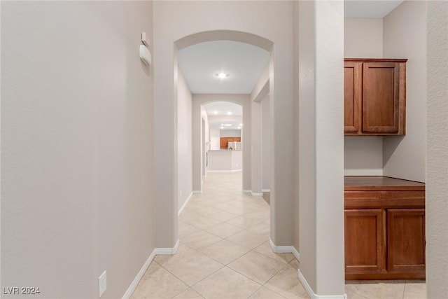 corridor featuring arched walkways, light tile patterned floors, and baseboards