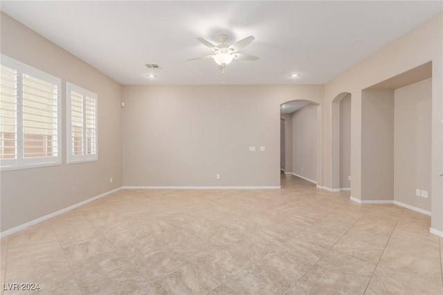 empty room with a ceiling fan, arched walkways, and baseboards