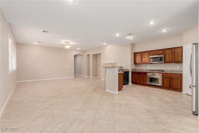 kitchen featuring arched walkways, brown cabinets, stainless steel appliances, light countertops, and open floor plan