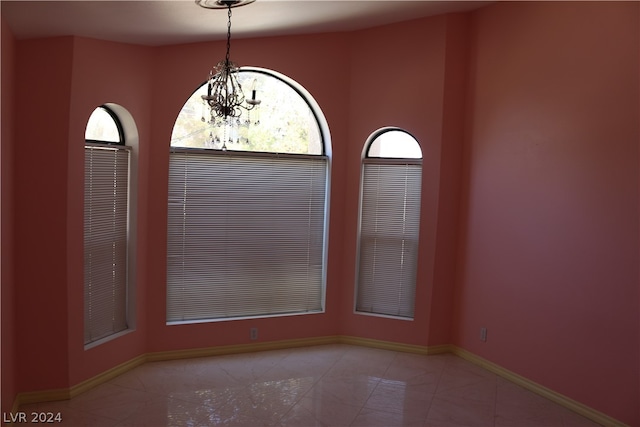 tiled empty room featuring an inviting chandelier