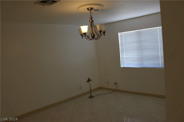 tiled spare room with an inviting chandelier