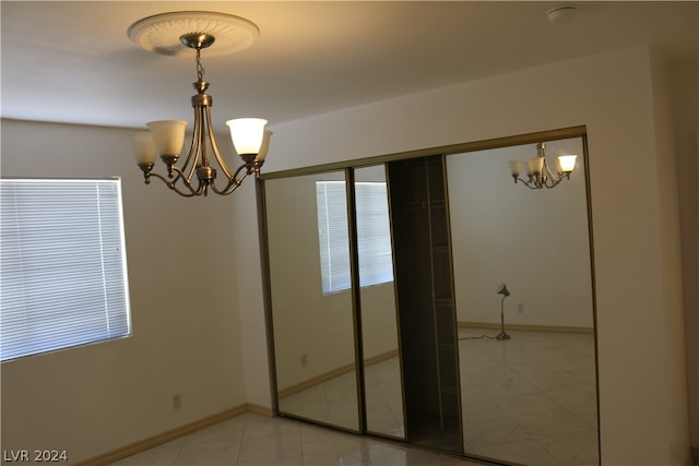 unfurnished bedroom with tile patterned flooring, a closet, and a notable chandelier