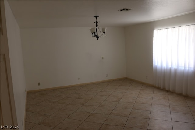 tiled spare room featuring a chandelier