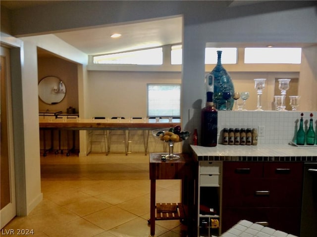 kitchen featuring tile countertops, lofted ceiling, light tile patterned floors, and backsplash