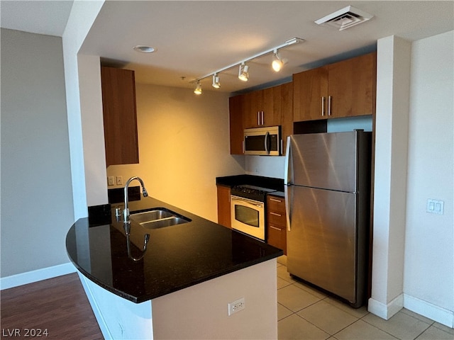 kitchen featuring light hardwood / wood-style flooring, kitchen peninsula, track lighting, appliances with stainless steel finishes, and sink