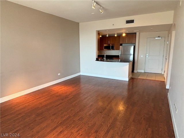 unfurnished living room with sink, hardwood / wood-style flooring, and rail lighting