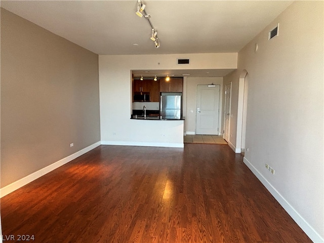 unfurnished living room featuring sink, rail lighting, and dark hardwood / wood-style floors