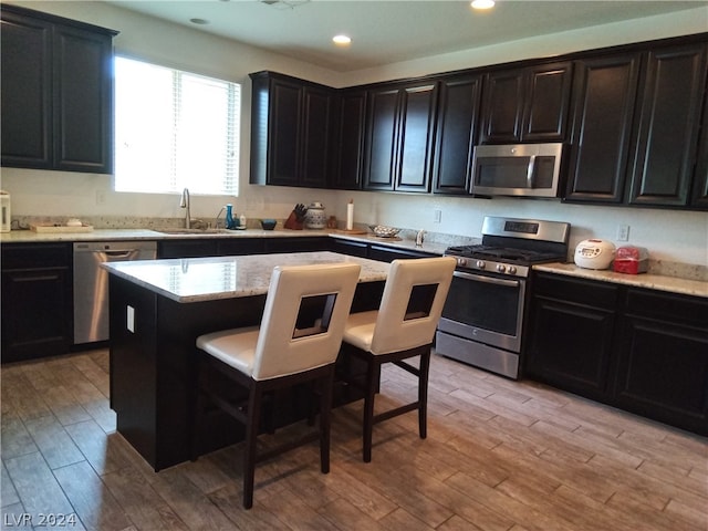 kitchen with a kitchen bar, stainless steel appliances, sink, light wood-type flooring, and a center island