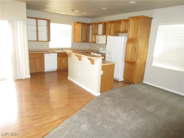 kitchen with sink, light hardwood / wood-style flooring, white appliances, a kitchen island, and a breakfast bar area