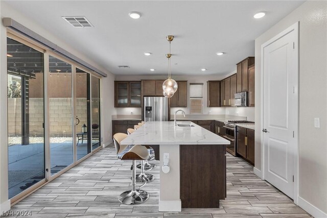 kitchen featuring a breakfast bar area, a kitchen island with sink, stainless steel appliances, decorative light fixtures, and sink