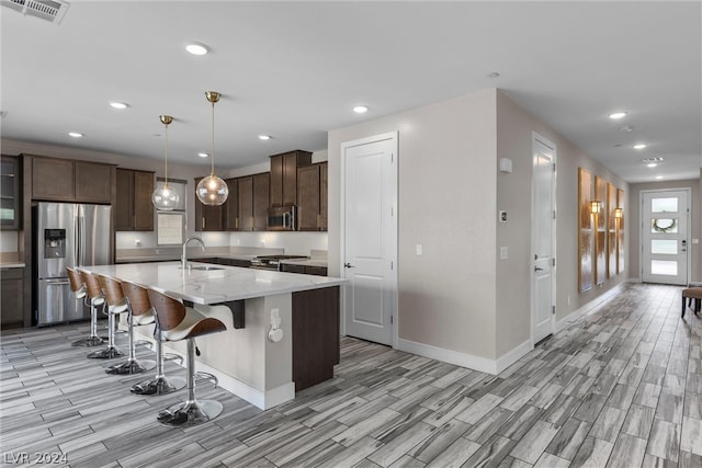 kitchen with light stone counters, stainless steel appliances, hanging light fixtures, sink, and a center island with sink