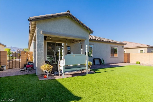 rear view of property with a tile roof, fence, a yard, a gate, and stucco siding