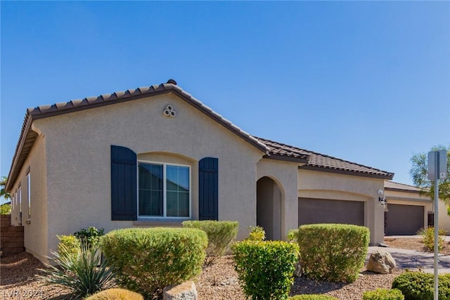 mediterranean / spanish-style home featuring a garage, driveway, a tiled roof, and stucco siding