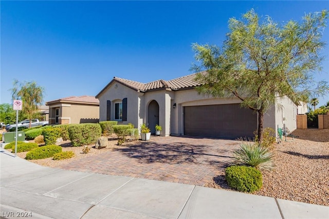 mediterranean / spanish-style home featuring decorative driveway, a tile roof, stucco siding, an attached garage, and fence