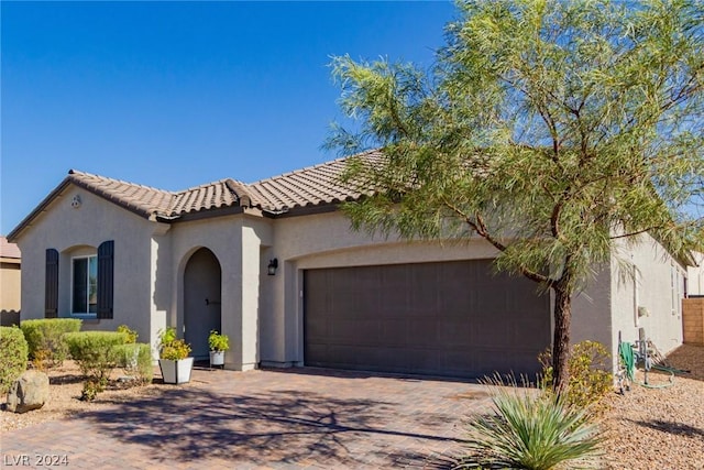 mediterranean / spanish home with decorative driveway, an attached garage, a tile roof, and stucco siding