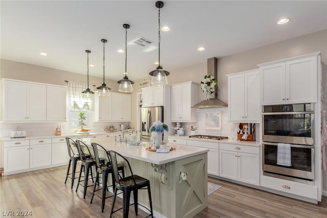 kitchen with a center island with sink, visible vents, stainless steel appliances, light countertops, and wall chimney range hood