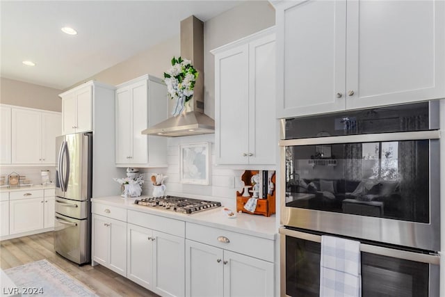 kitchen with white cabinets, wall chimney range hood, appliances with stainless steel finishes, and light countertops