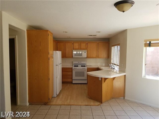 kitchen with light wood-type flooring, white appliances, sink, kitchen peninsula, and a kitchen breakfast bar