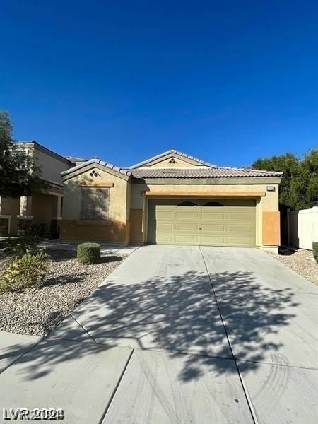 ranch-style house with concrete driveway, a tiled roof, a garage, and stucco siding