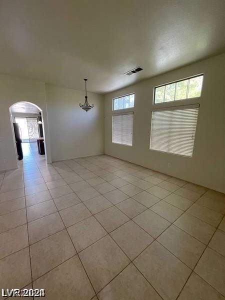 empty room featuring light tile patterned floors, visible vents, and arched walkways