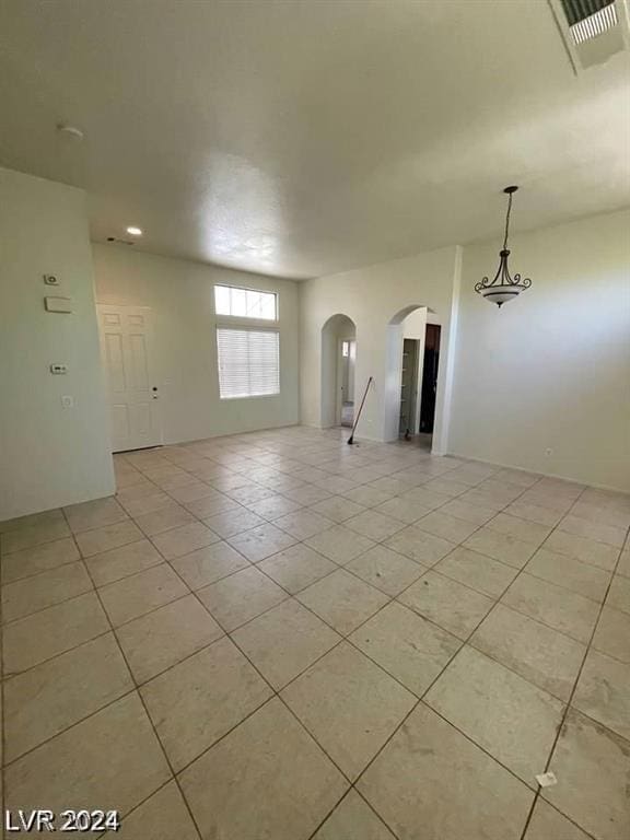 unfurnished room with light tile patterned floors, visible vents, and arched walkways