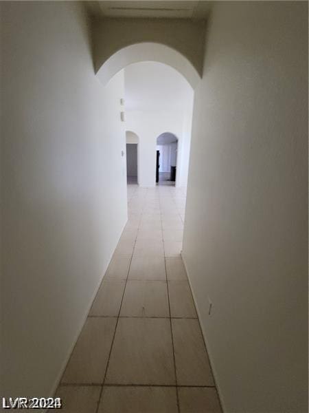 hall with light tile patterned floors, baseboards, and arched walkways