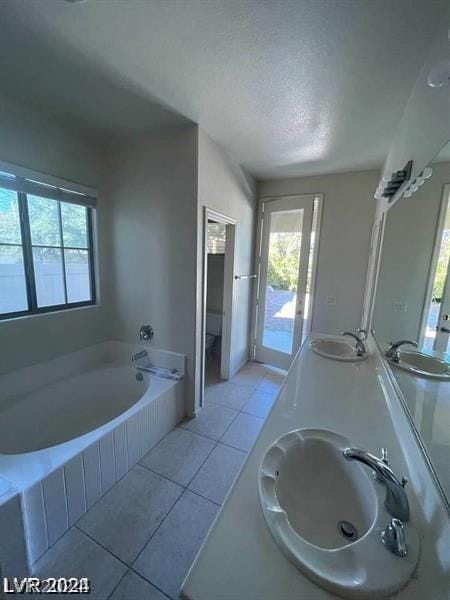 full bath featuring a sink, a garden tub, a textured ceiling, and tile patterned flooring